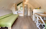 Vue intérieure d'une pod moderne et cosy avec canapé vert, table à manger, cuisine et coin nuit.