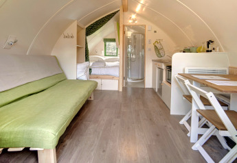 Interieur van een gezellige, moderne pod met groene zetel, eettafel, compacte keuken en slaaphoek.
