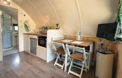 Pod moderne avec coin cuisine, table à manger pour deux, télé murale et salle de bain avec douche.