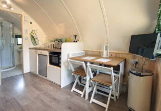 Moderne pod met kitchenette, eettafel, twee stoelen, wand-tv en een badkamer met douche op de achtergrond.