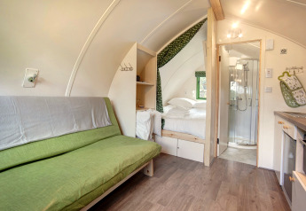 Binnenkant van een knusse pod bij Barebones Glamping in het VK met zitbank, bed en badkamer.