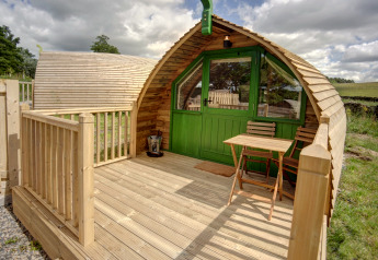 Houten terras met tafel en stoelen bij een Barebones Glamping pod met groene deur in het Britse landschap.