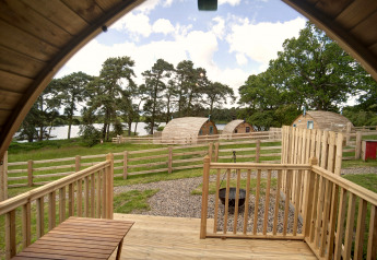 Zicht vanuit een houten pod op Barebones Glamping, VK, met houten hekjes en een meer.