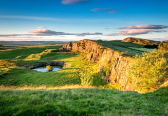 Mooie landschapsfoto van een poel omringd door groene weiden en rotsen onder een blauwe lucht.