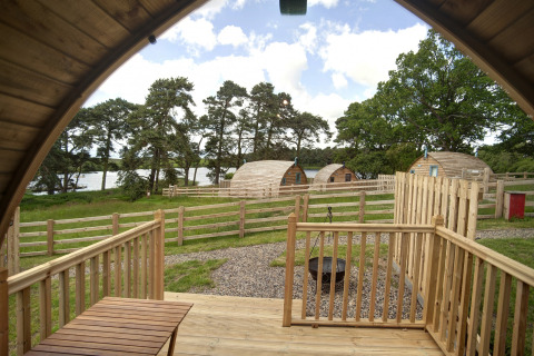 Uitzicht vanaf de veranda van The Rushy Lot pod in het VK, met houten huisjes, hekjes en groen landschap.
