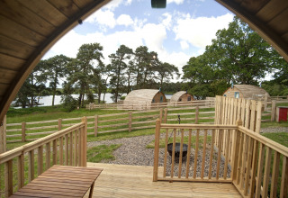 Uitzicht vanaf de veranda van The Rushy Lot pod in het VK, met houten huisjes, hekjes en groen landschap.