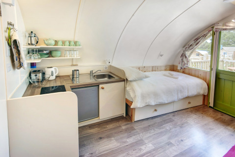 Interieur van Humbleton Glamping pod in het VK met comfortabel bed, kleine keuken en groene deur.
