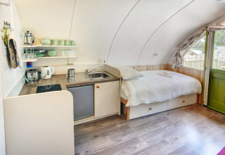 Interieur van Humbleton Glamping pod in het VK met comfortabel bed, kleine keuken en groene deur.