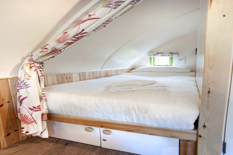 Knus slaapvertrek met tweepersoonsbed, witte lakens en bloemgordijn bij Humbleton Glamping, Verenigd Koninkrijk.