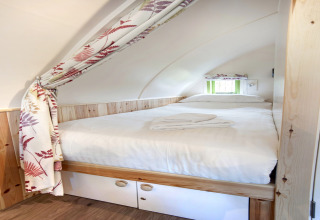 Knus slaapvertrek met tweepersoonsbed, witte lakens en bloemgordijn bij Humbleton Glamping, Verenigd Koninkrijk.