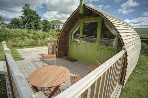 Houten terras met tafel en stoelen voor een gebogen glampingpod bij Humbleton Glamping, Verenigd Koninkrijk.
