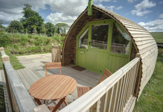 Houten terras met tafel en stoelen voor een gebogen glampingpod bij Humbleton Glamping, Verenigd Koninkrijk.