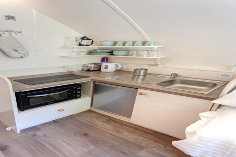 Kleine kitchenette bij Humbleton Glamping in het VK met kookplaat, gootsteen, magnetron en open planken.