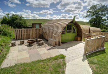 Houten glampingpod met groene deur bij Humbleton Glamping, Verenigd Koninkrijk, omgeven door natuur.