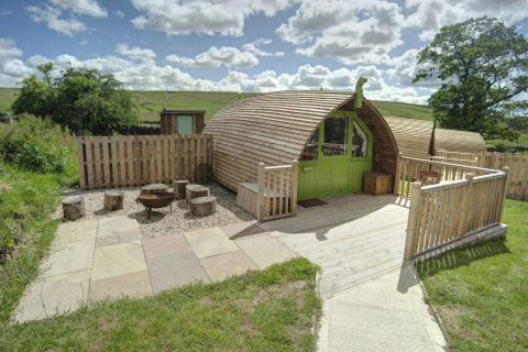 Houten glampingpod met groene deur bij Humbleton Glamping, Verenigd Koninkrijk, omgeven door natuur.