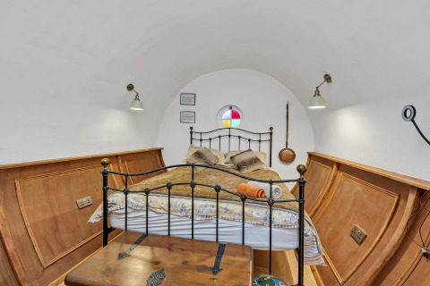 Camera da letto nel Pod 'Hollow' con soffitto curvo, letto in ferro, pannelli in legno e finestra rotonda colorata nel Regno Unito.