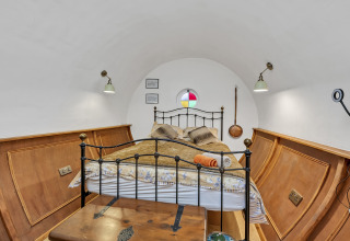 Camera da letto nel Pod 'Hollow' con soffitto curvo, letto in ferro, pannelli in legno e finestra rotonda colorata nel Regno Unito.