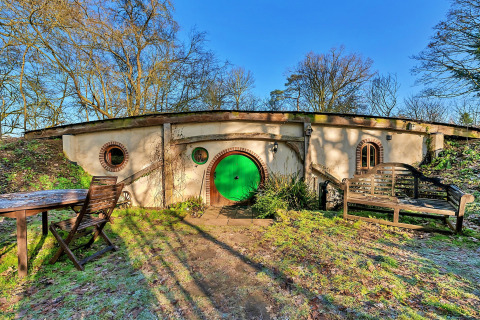 Vista esterna del pod 'Hollow' nel Regno Unito, con porta verde rotonda, arredi da esterno e scenario naturale.