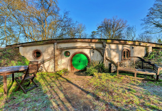 Vista esterna del pod 'Hollow' nel Regno Unito, con porta verde rotonda, arredi da esterno e scenario naturale.