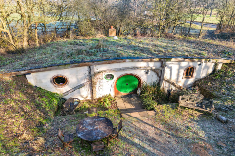 Pod Hollow, una casa sotterranea in stile hobbit con tetto erboso e porta d’ingresso rotonda verde.