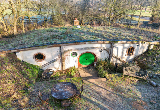 Pod Hollow, una casa sotterranea in stile hobbit con tetto erboso e porta d’ingresso rotonda verde.