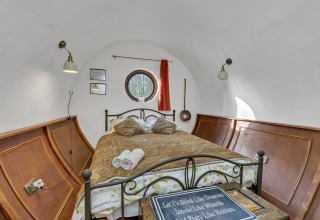 Accogliente stanza pod nel Regno Unito con pareti curve, letto matrimoniale, pannelli in legno e finestra tonda.