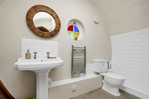 Bagno nel Pod 'Hollow' nel Regno Unito con piastrelle bianche, finestra rotonda e specchio in legno.