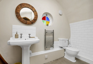 Bagno nel Pod 'Hollow' nel Regno Unito con piastrelle bianche, finestra rotonda e specchio in legno.