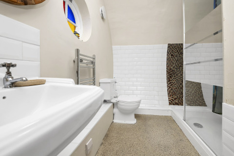 Bagno di Pod Hollow con doccia moderna, WC, lavabo e finestra rotonda colorata, Regno Unito.