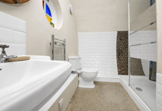 Bagno di Pod Hollow con doccia moderna, WC, lavabo e finestra rotonda colorata, Regno Unito.