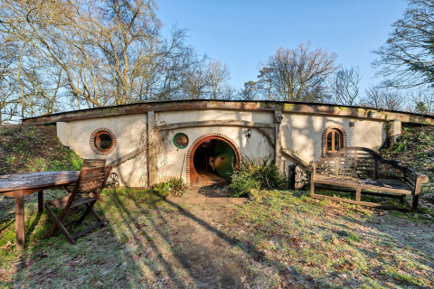Vista esterna di Pod 'Hollow', una capanna sotterranea con porta e finestre rotonde nel Regno Unito.
