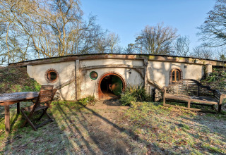 Vista esterna di Pod 'Hollow', una capanna sotterranea con porta e finestre rotonde nel Regno Unito.