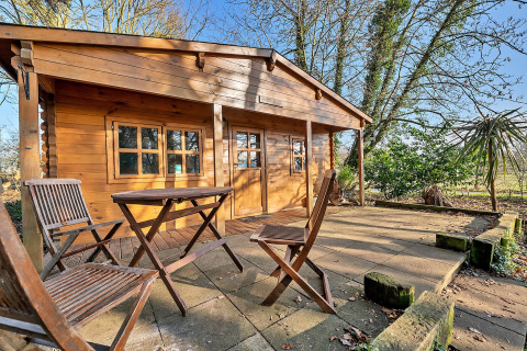 Woodland Lodge chalet in the UK with wooden chairs and table on the patio, surrounded by nature.