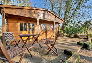 Woodland Lodge chalet in the UK with wooden chairs and table on the patio, surrounded by nature.