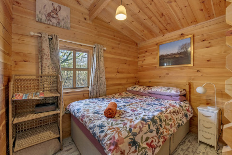Woodland Lodge bedroom in the UK with a wooden interior, double bed, nature decor, and a window view.