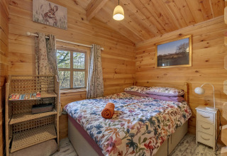 Woodland Lodge bedroom in the UK with a wooden interior, double bed, nature decor, and a window view.