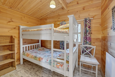 Bedroom at Woodland Lodge chalet in the UK featuring a bunk bed, wooden walls, shelving, and floral curtains.