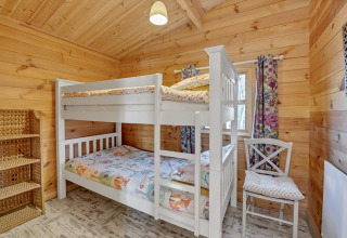 Bedroom at Woodland Lodge chalet in the UK featuring a bunk bed, wooden walls, shelving, and floral curtains.