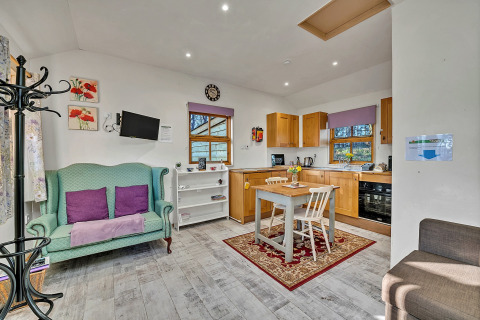 Lys og hyggelig stue og køkken i Cedar Lodge chalet, med grøn sofa, spisebord og træskabe.