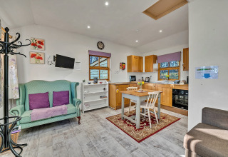Lys og hyggelig stue og køkken i Cedar Lodge chalet, med grøn sofa, spisebord og træskabe.
