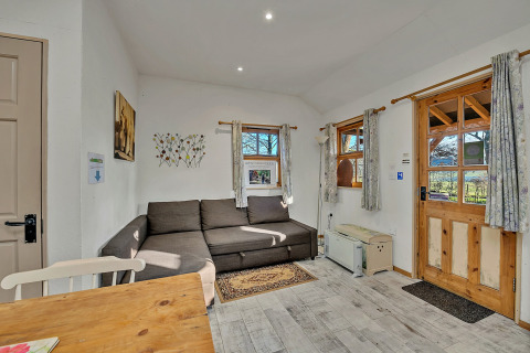 Stue i Cedar Lodge chalet med hjørnesofa, trædør, små vinduer og lyse gardiner, Storbritannien.