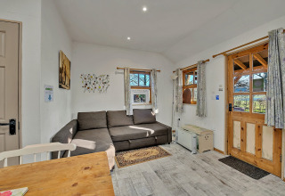 Stue i Cedar Lodge chalet med hjørnesofa, trædør, små vinduer og lyse gardiner, Storbritannien.