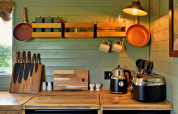 Modern mobile home kitchen with wooden counters, pans, knives, and appliances in 'Joan' Shepherds Hut, UK.