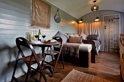 Knusse woonwagen met houten interieur, eethoek, wijn en bed in ‘Joan’ Shepherds Hut, Verenigd Koninkrijk.