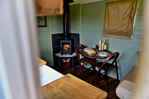 Knusse eethoek in de 'Joan' Shepherds Hut mobilhome met houtkachel, tafel en stoelen in het Verenigd Koninkrijk.
