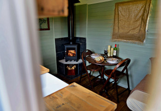 Knusse eethoek in de 'Joan' Shepherds Hut mobilhome met houtkachel, tafel en stoelen in het Verenigd Koninkrijk.
