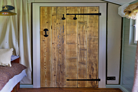 Interieurbeeld van een rustieke houten deur met zwart beslag in 'Joan' Shepherds Hut, Verenigd Koninkrijk.