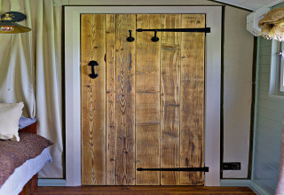 Interieurbeeld van een rustieke houten deur met zwart beslag in 'Joan' Shepherds Hut, Verenigd Koninkrijk.