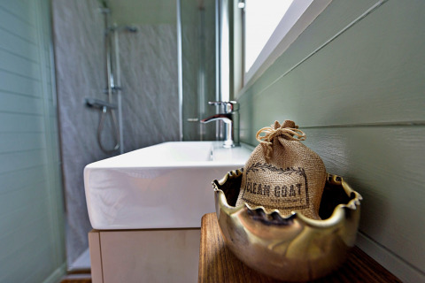 Moderne badkamer in de 'Joan' Shepherds Hut, met wastafel en decoratief zakje op houten tafeltje.