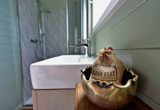 Moderne badkamer in de 'Joan' Shepherds Hut, met wastafel en decoratief zakje op houten tafeltje.